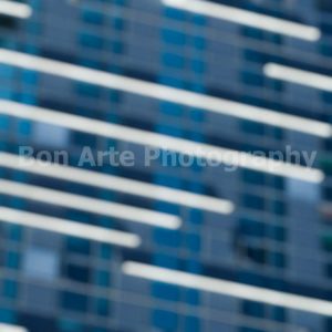 A heavily bokeh out of focus close up of a abstract blue glass skyscraper facade with dynamic bright white diagonal light streaks and motion blur lines for electronic music album cover photography by Bon Arte Photography.