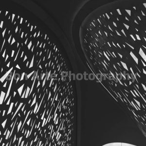 A minimalist square composition of a modern architectural structure featuring a complex lattice pattern of geometric cutouts with light passing through, ideal for electronic music album artwork.