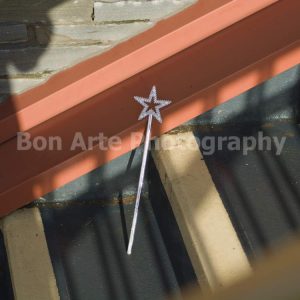 A moody emo pop photo showcasing a silver glitter star wand abandoned on raw concrete steps under sharp sun shadows by Bon Arte Photography.