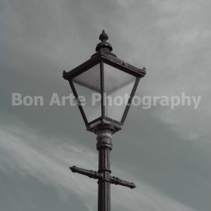 A grayscale antique Victorian street lantern silhouette isolated against a dramatic overcast sky with ample layout copy space for a thriller book title.