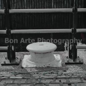 A gritty harbor crime book cover stock photo featuring an industrial port mooring bollard and metal railing on a cobblestone pier for thriller design by Bon Arte Photography.