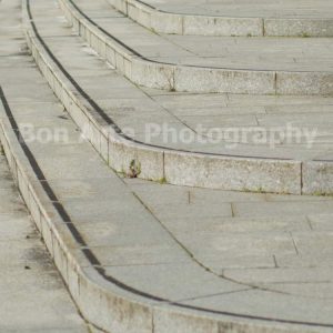 A minimalist square fine art photograph focusing on the sweeping lines of curved outdoor concrete steps and stone stairs, perfect for an electronic music album cover layout.