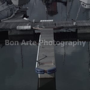 A minimalist marina dock in a quiet harbor surrounded by boats with water reflections, ideal for dark thriller book cover layouts.