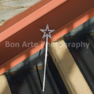 A gritty mystery wand book cover stock photo featuring a silver glitter star wand abandoned on concrete steps under sharp sun shadows by Bon Arte Photography.