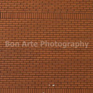A massive flat orange-red brick wall texture with a vertical brick border pattern and a distressed metallic Private notice sign at the very bottom center for crime fiction book cover photography by Bon Arte Photography.