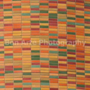 A vibrant square fine art photograph capturing a pattern of small rectangular ceramic mosaic tiles in retro orange, green, yellow, and red earth tones, ideal for a vinyl album cover design.