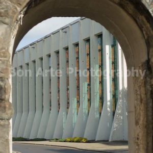 An old weathered stone arch framing a modern brutalist concrete building with repeated glass vertical windows and structural pillars under bright daylight for thriller novel book cover photography by Bon Arte Photography.