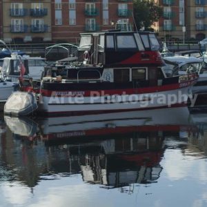 A moody red and black trawler boat named Zebulin Queen docked in a harbor with reflections in the water for a mystery novel background book cover photography by Bon Arte Photography.